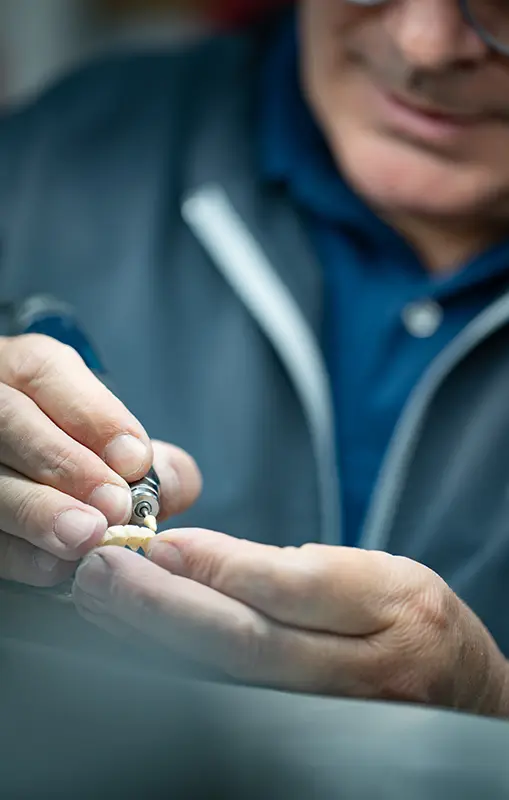 Main d'un artisan prothésiste dentaire effectuant les finitions manuelles sur une prothèse.
