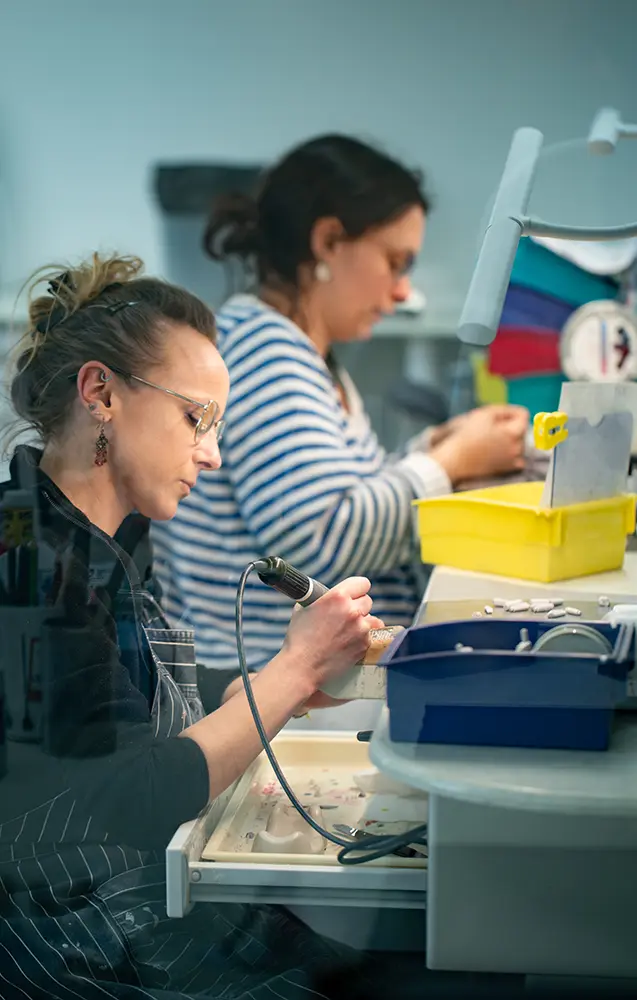 Collaboratrices du Laboratoire 32 effectuant minutieusement les finitions artisanales sur des prothèses dentaires à leur poste de travail.